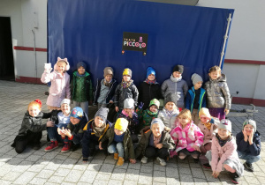 Gupa dzieci pozujących do zdjęcia przy plandece z napisem teatr Piccolo