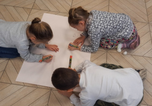 Trójka dzieci rysuje wspólnie na dużym kartonie.
