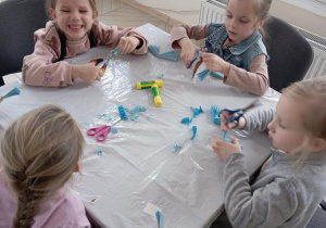 Dzieci siedzą przy stoliku i wykonują prace plastyczną.