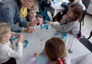 Dzieci siedzą przy stoliku i wykonują prace plastyczną.