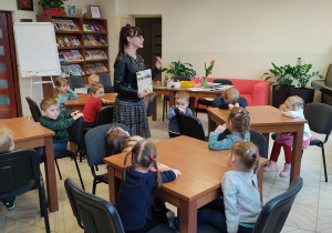 Dzieci słuchają czytanego wiersza przez Bibliotekarkę