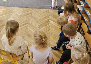 Dzieci siedzą na krzesełkach oczekując na swoją kolej w zabawie tor przeszkód