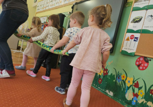 Dzieci z nauczycielką wędrują po sali z pluszowym wężem