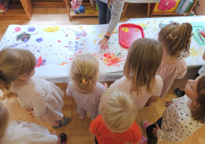 Dzieci przyglądają się jak nauczycielka prezentuje wykonanie pracy plastycznej