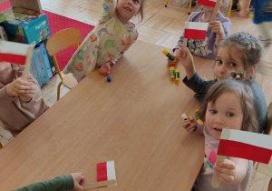 Dzieci siedzące przy stoliku z flagami Polski.