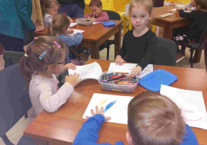 Dzieci siedzą przy stoliku i rysują.