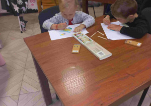 Dzieci siedzą przy stoliku i rysują.