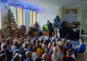 Dzieci siedzą na dywanie i słuchają, jak Panie śpiewają piosenki świąteczne.
