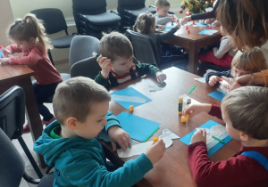 Dzieci siedzą przy stoliku i wykonują zimowe prace plastyczne.