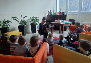 Dzieci słuchają książki czytanej przez Panią bibliotekarkę.