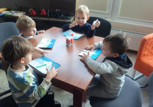 Dzieci siedzą przy stoliku i wykonują zimowe prace plastyczne.
