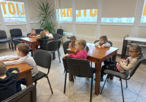 Dzieci siedzą przy stoliku i słuchają Pani z biblioteki.